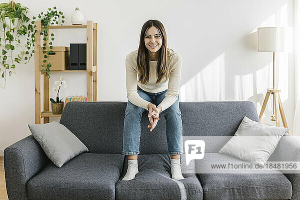 Glückliche junge Frau sitzt auf dem Sofa im Wohnzimmer