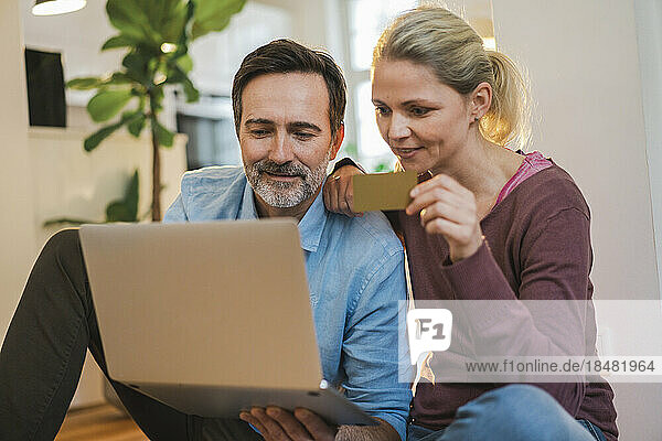 Woman holding credit card by man using laptop at home