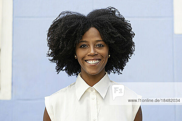 Happy woman with Afro hairstyle standing in front of wall