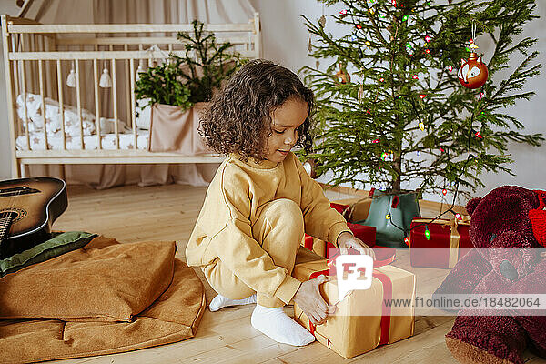 Cute girl opening gifts iunder Christmas tree at home