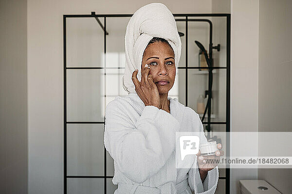 Woman applying moisturizer on face in bathroom at home
