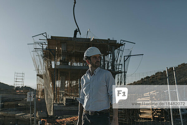 Contemplative architect wearing hardhat standing at construction site