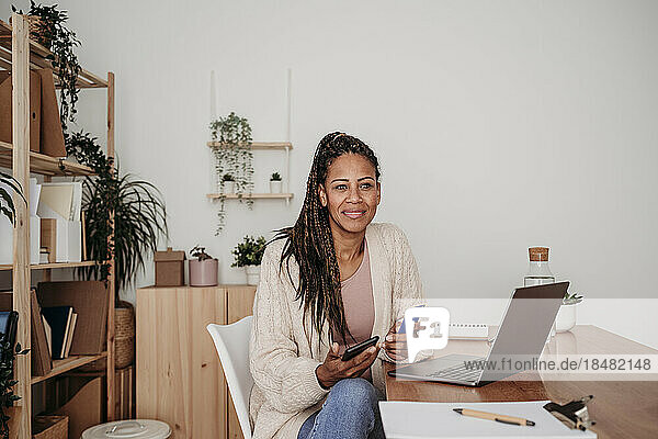 Smiling freelancer with credit card and smart phone sitting at home office