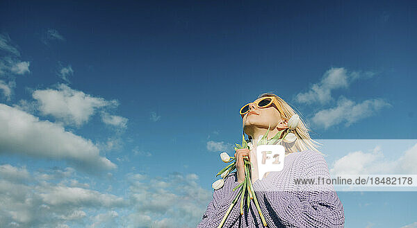 Frau mit Sonnenbrille steht mit Tulpen unter blauem Himmel