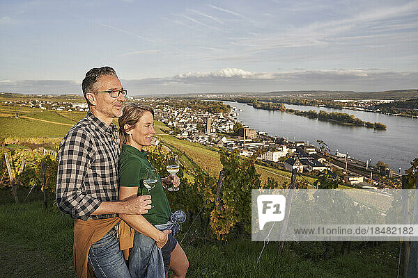 Mature couple standing with wineglasses looking at river