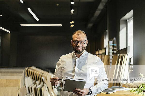 Portrait of smiling businessman holding book in architect's office