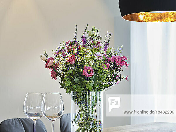 Fresh flower vase by wineglasses in apartment