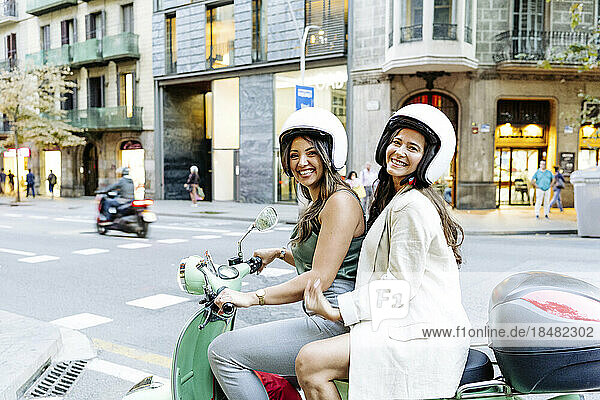 Happy friends sitting on electric scooter in front of building