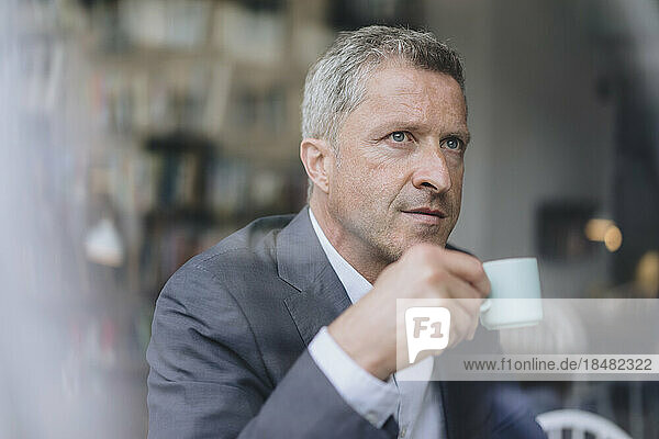 Thoughtful businessman with coffee cup seen through glass window