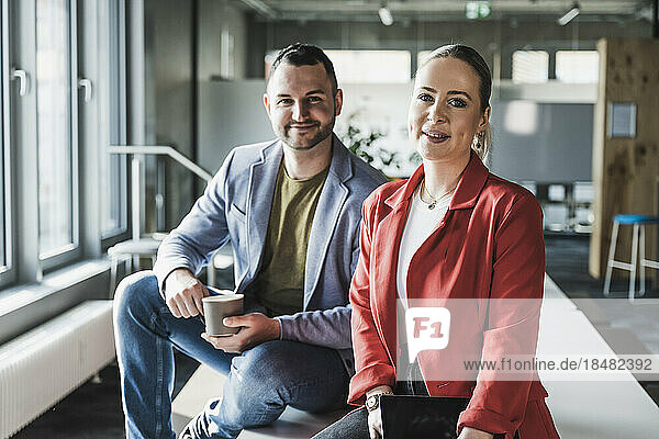 Smiling business colleagues sitting on desk in office