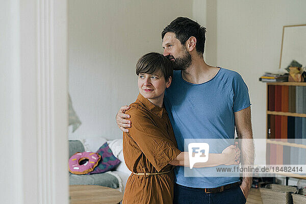 Romantic man with arm around woman standing at home