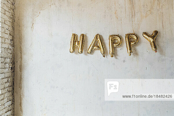 Gold colored happy text made with inflated balloons hanging on wall