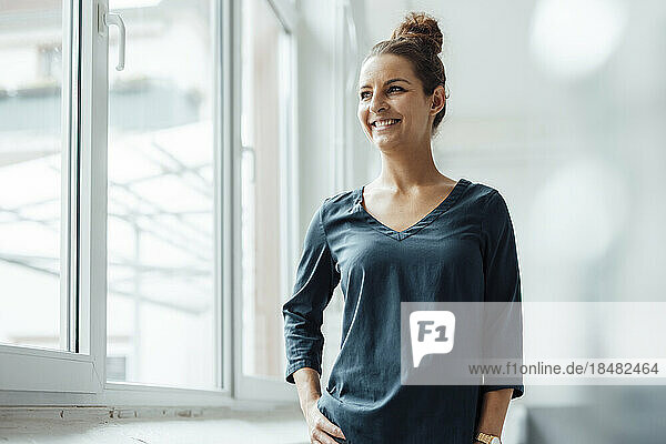 Happy businesswoman standing with hand on hip at home office