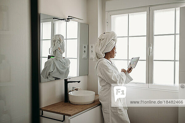 Mature woman using tablet PC in bathroom at home