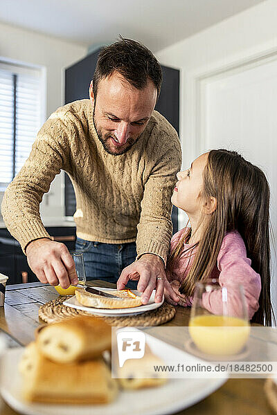 Lächelnder Vater serviert seiner Tochter am Tisch Frühstück