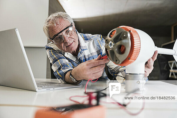 Technician examining wind turbine rotor on desk at office
