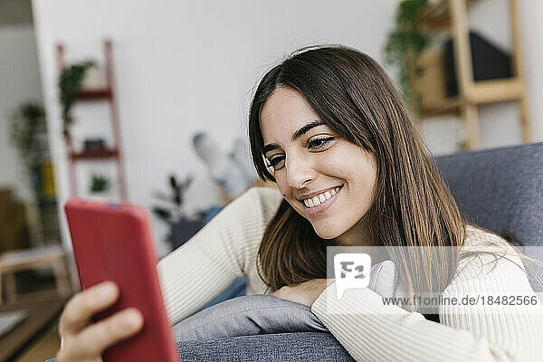 Happy woman text messaging through smart phone in living room