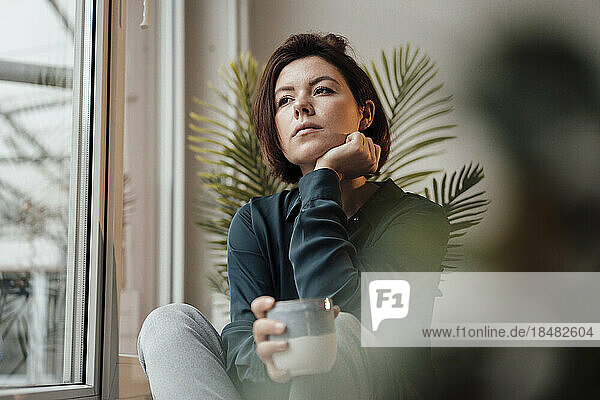 Thoughtful businesswoman with coffee cup sitting near window