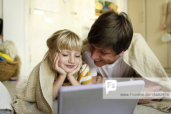 Smiling father with daughter watching tablet PC lying on floor at home