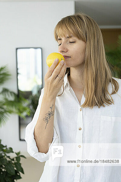 Woman with eyes closed smelling lemon at home
