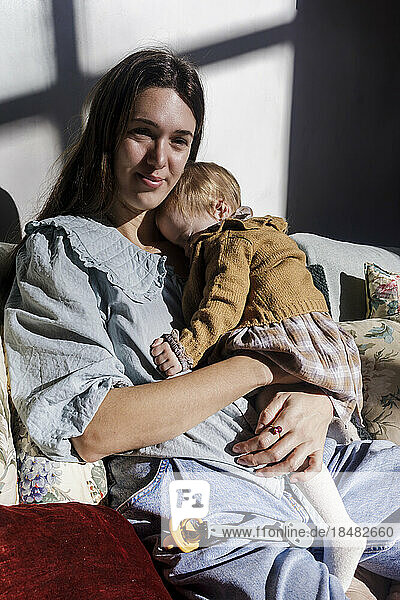 Smiling mother with baby girl sitting on sofa in sunlight
