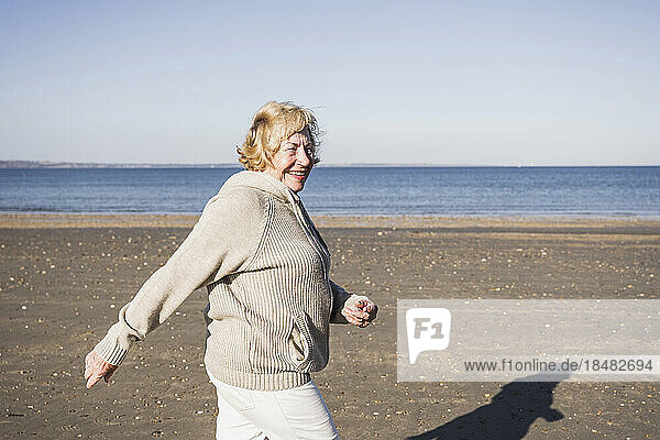 Lächelnde ältere Frau  die am Strand am Meer entlang spaziert