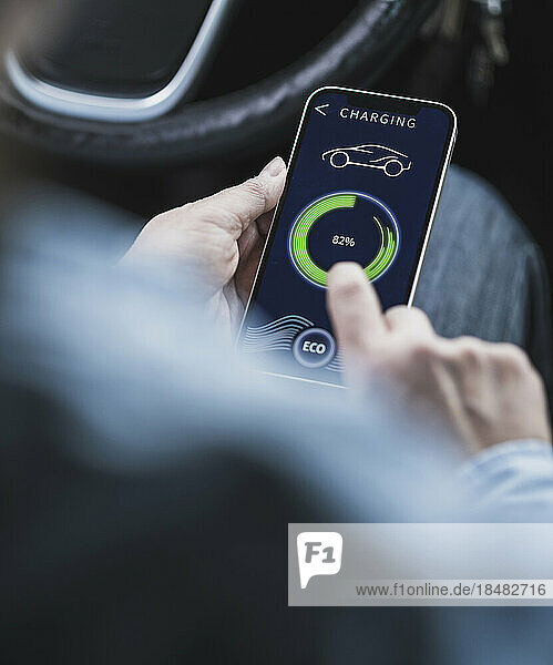 Hands of mature woman using mobile app to operate electric car