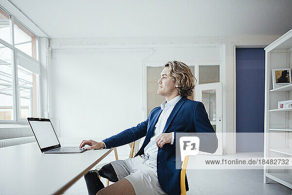 Nachdenklicher Geschäftsmann sitzt mit Laptop im Büro