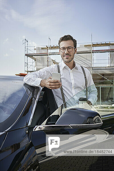 Architect standing with smart phone by car at construction site