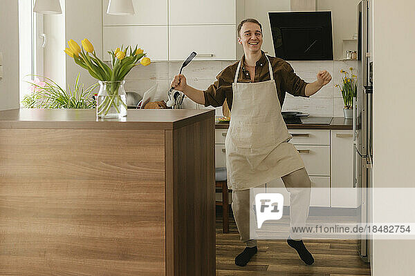 Sorgloser Mann hält Spatel in der heimischen Küche und tanzt