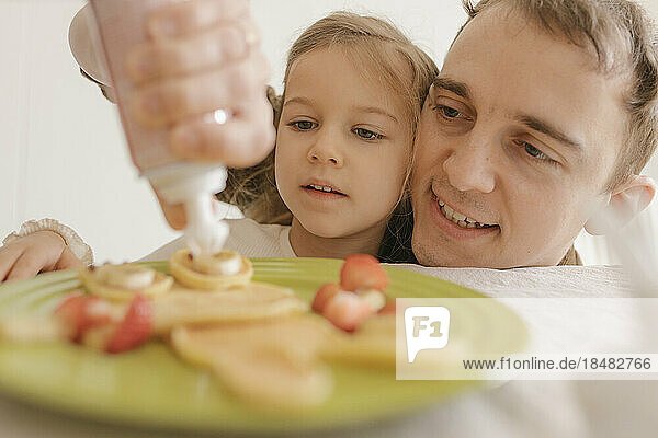Happy father and daughter decorating pancake on plate at home