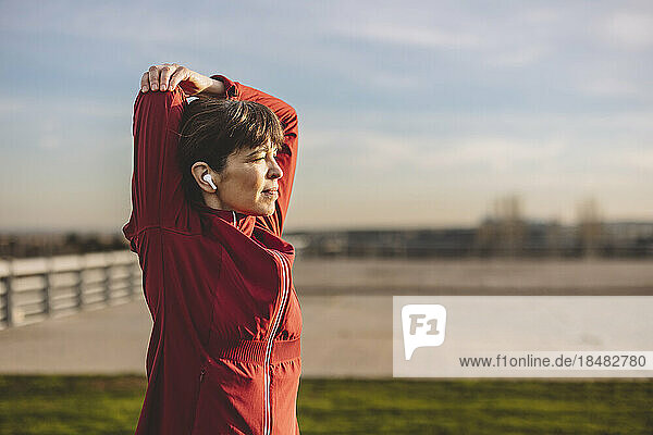 Mature woman stretching arms on sunny day