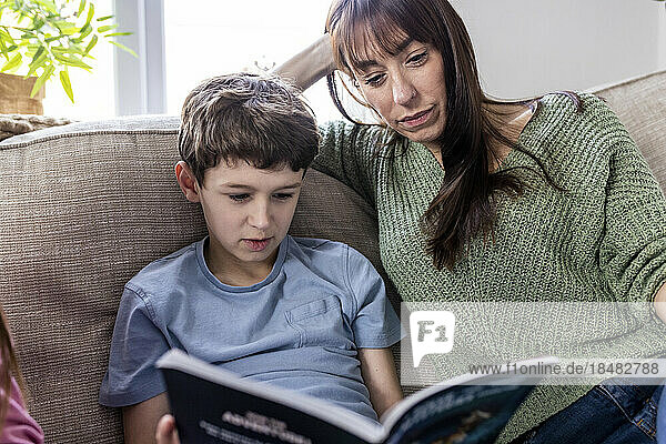 Frau liest Buch mit Sohn auf Sofa zu Hause
