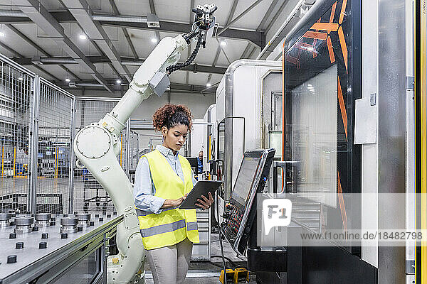 Young engineer using tablet PC by robotic arm at industry