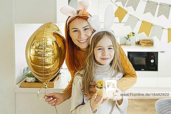 Glückliches Mädchen mit Mutter  die zu Hause einen Ballon feiert und Ostern feiert