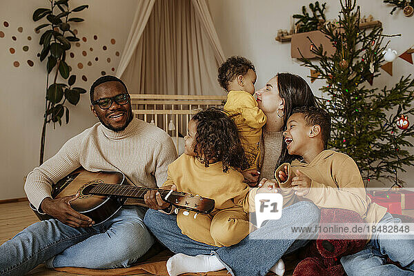 Fröhliche Familie verbringt zu Weihnachten Zeit miteinander und spielt Gitarre
