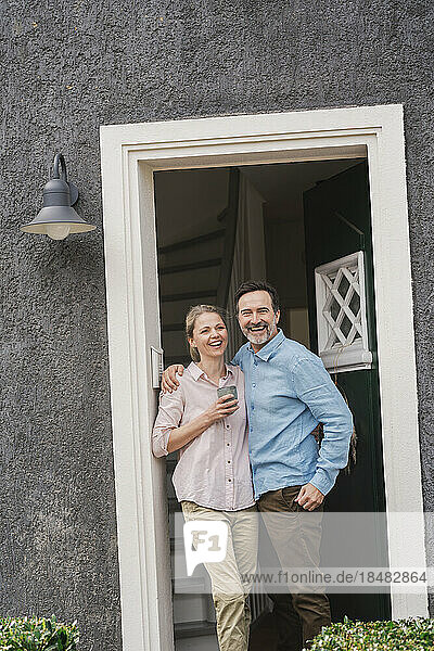 Cheerful mature couple standing at doorway of house