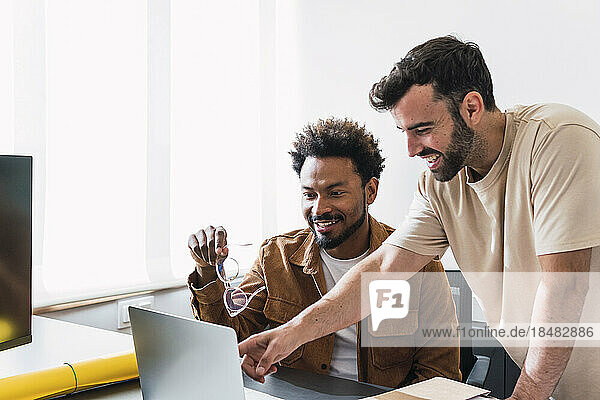 Happy businessman discussing with colleague over laptop in office