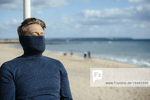 Mann trägt Rollkragenpullover  der sein Gesicht am Strand bedeckt
