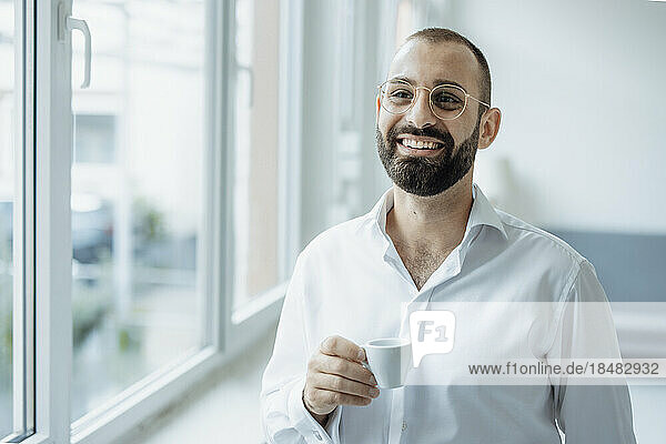 Happy businessman with cup of coffee standing at home office