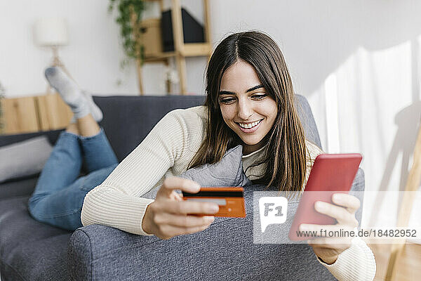 Happy woman with credit card doing shopping on smart phone at home