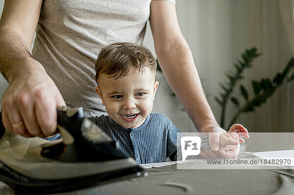 Glücklicher Junge genießt es  zu Hause mit seinem Vater Kleidung zu bügeln