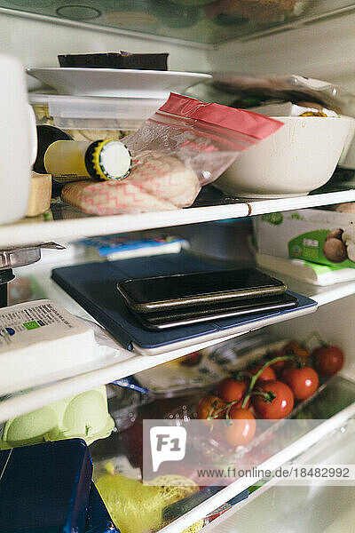 Smart phone and tablet PC with food stacked on shelf in refrigerator