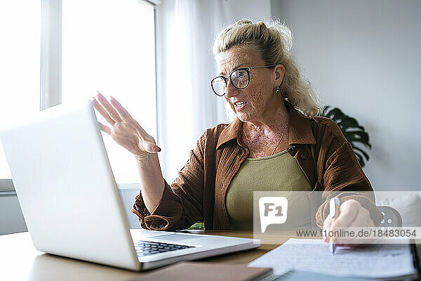 Businesswoman talking on video call through laptop at desk in home office
