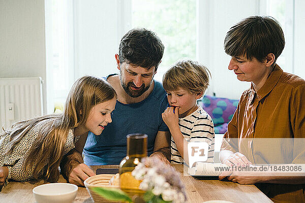 Familie schaut gemeinsam am Esstisch zu Hause auf den Tablet-PC