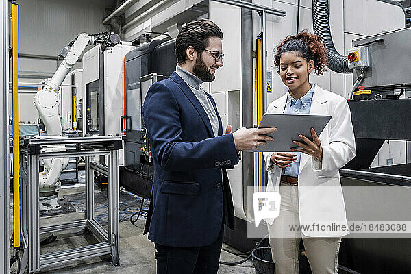 Businessman with colleague discussing over tablet PC in factory