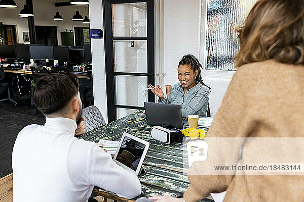 Smiling businesswoman showing wind turbine model to coworkers in office