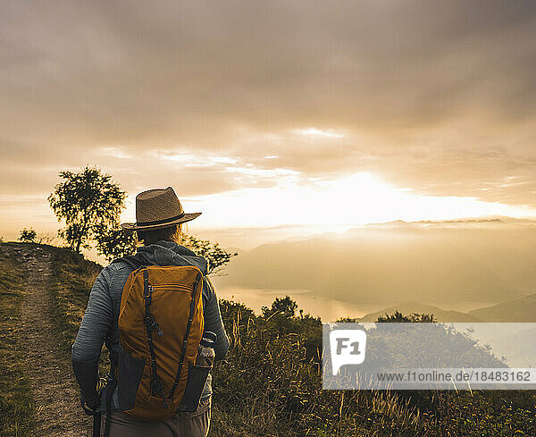 Frau mit Hut wandert bei Sonnenuntergang auf dem Berg