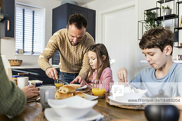 Vater trägt Butter auf Brot auf  während die Familie in der Küche frühstückt
