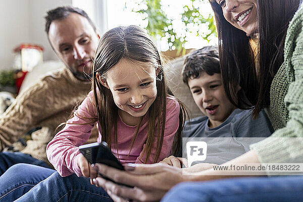 Happy girl using smart phone with family sitting on sofa at home